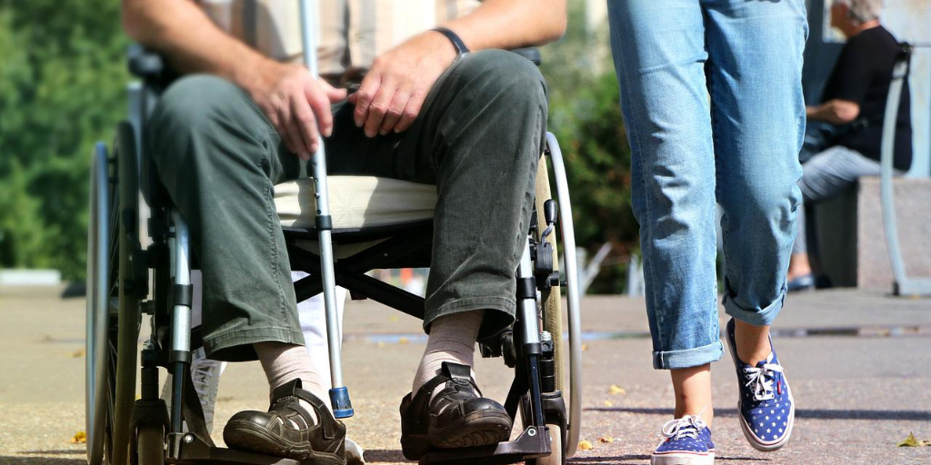 An older person on an armchair and a young person walking next to them, both cut to only show the bottom half of their bodies